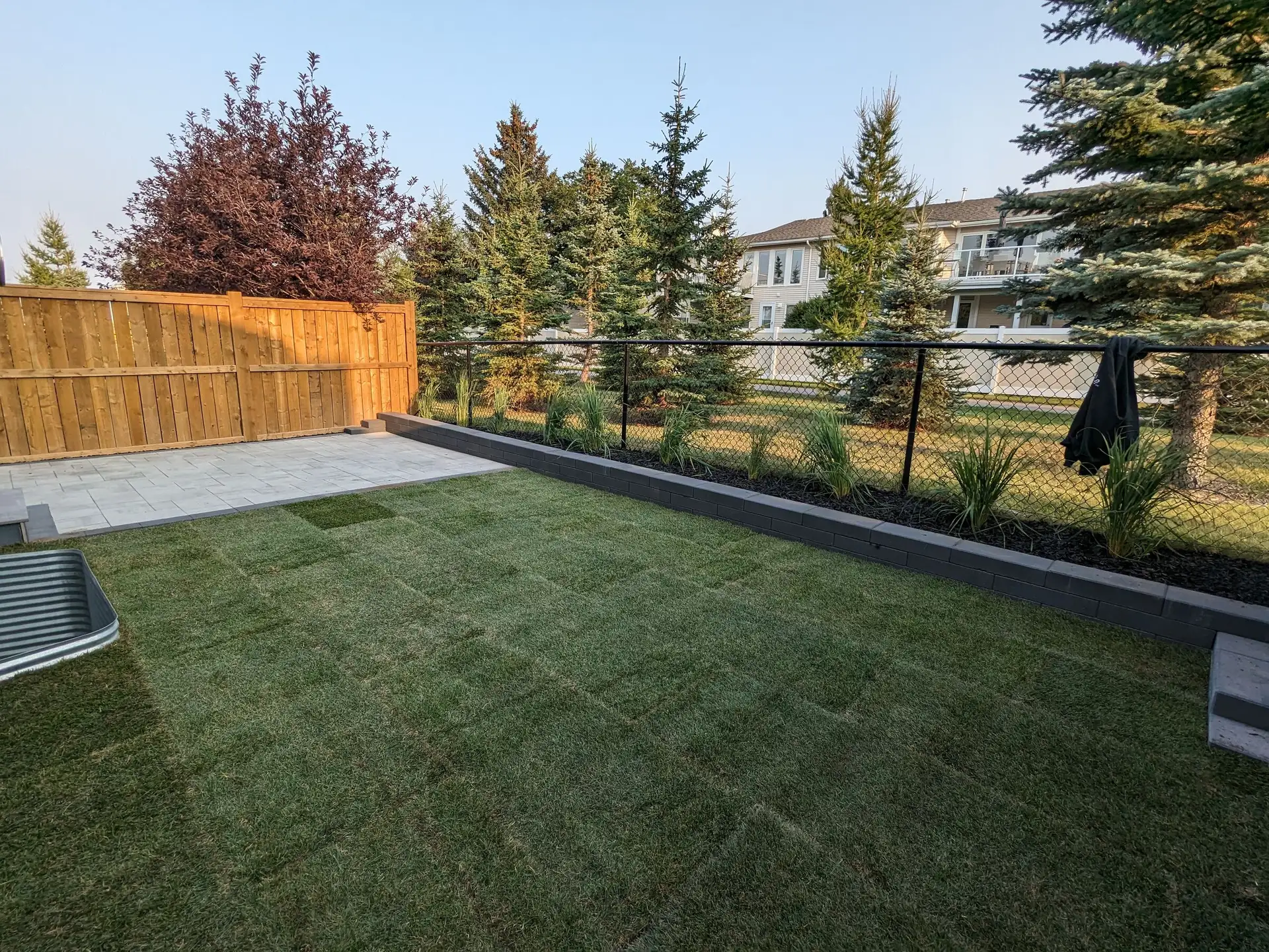 New sod, a paver patio and a low block wall holding a planted bed along a chain-link fence