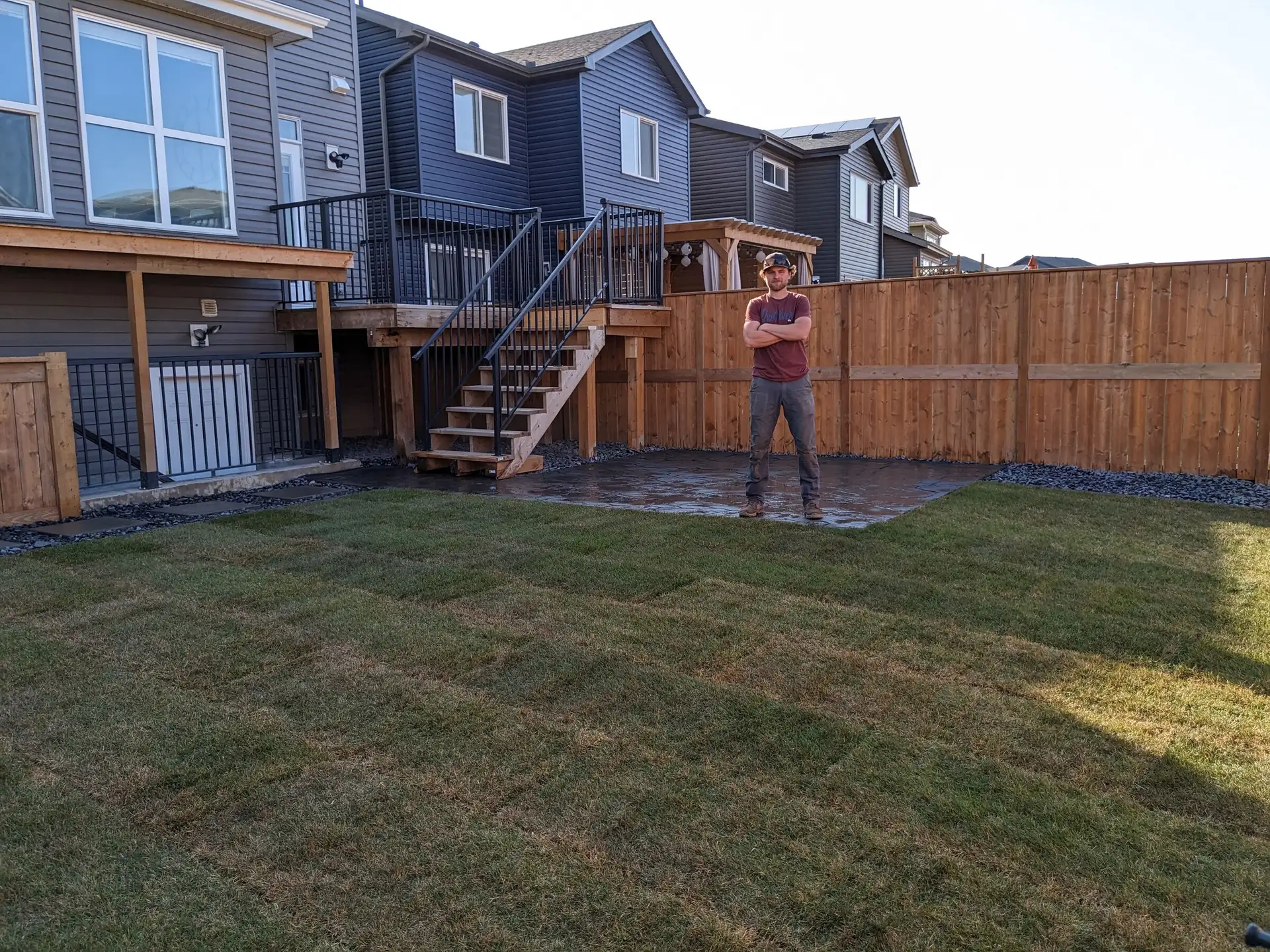 Owner Nick Roseboom standing on a finished job: freshly laid sod and a paver patio under a new deck