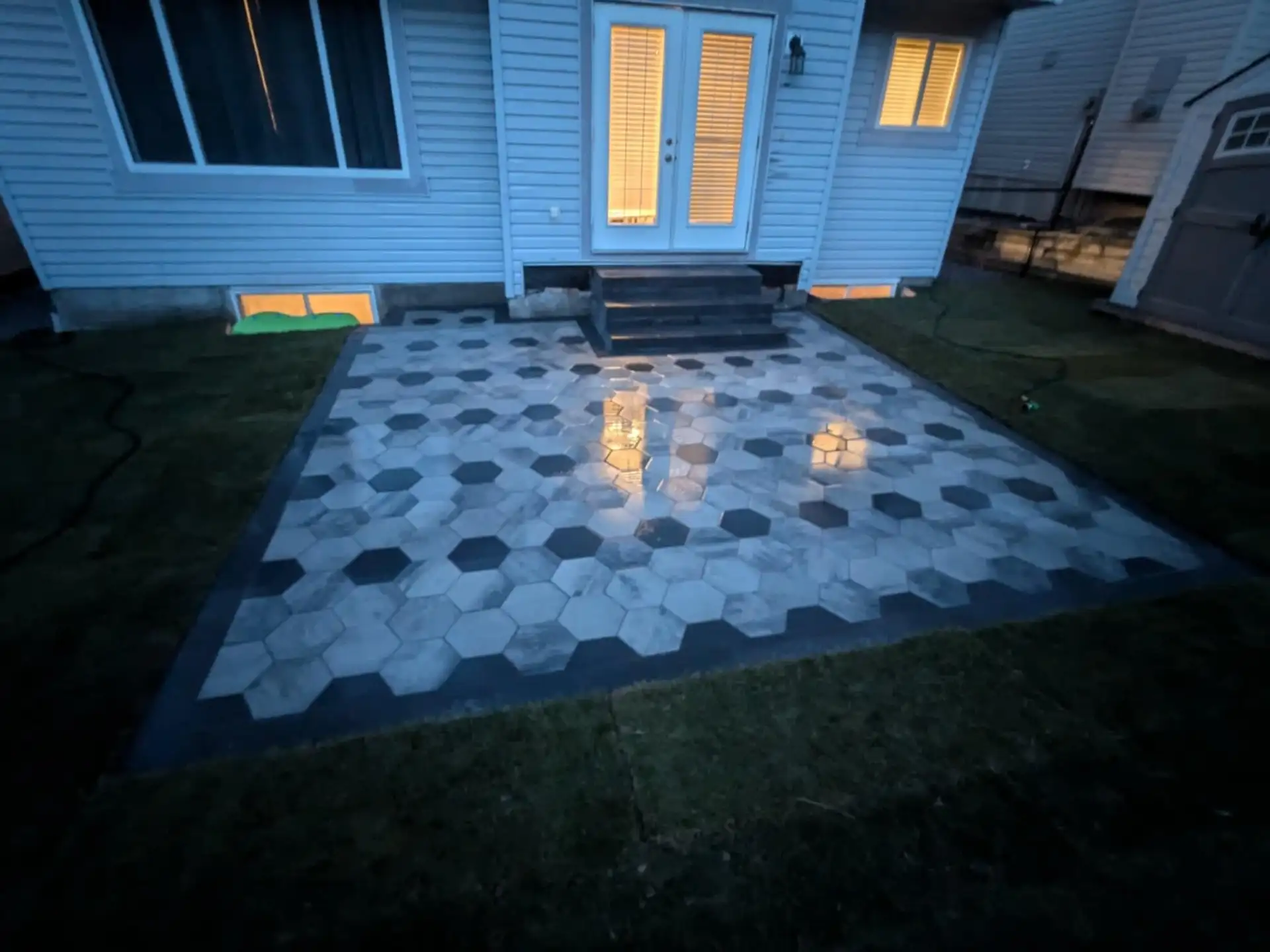 Hexagon paver patio in grey and charcoal, lit at dusk, leading to the back door steps