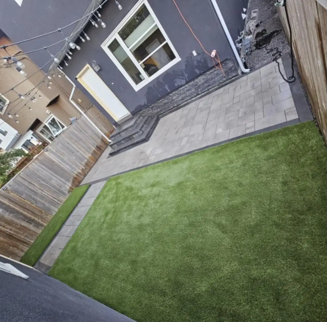 Artificial turf beside a large paver patio with built-in steps, seen from above