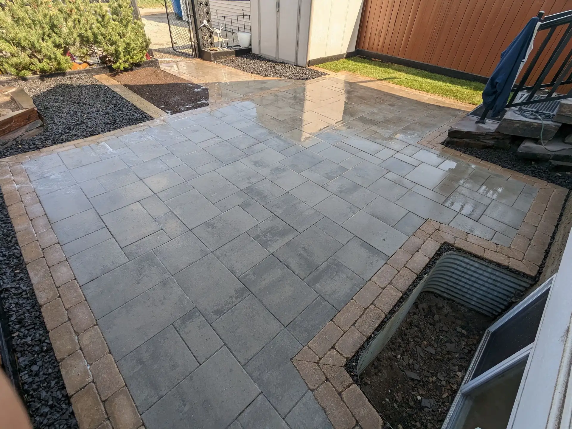 Grey paver patio with a tan soldier-course border wrapping around a window well
