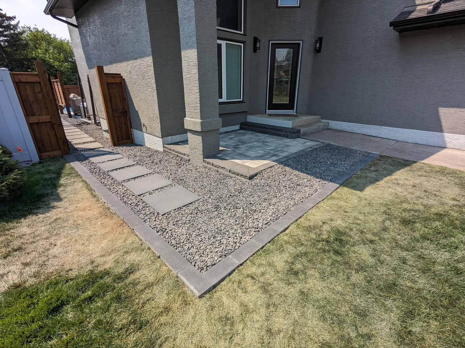Side yard with decorative gravel, slab stepping stones and a paver landing edged in charcoal